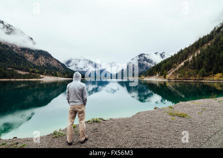 Rear view of a man wearing a hoodie looking at Plansee Lake located in Tirol, Austria. Stock Photo