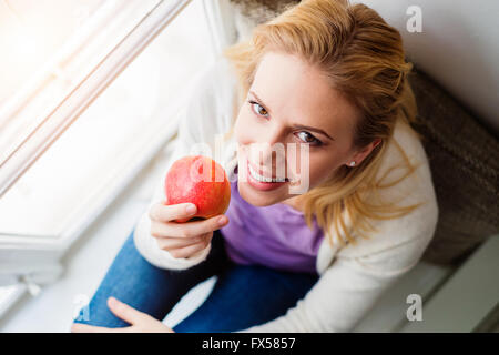 Woman on window sill holding fresh red apple Stock Photo