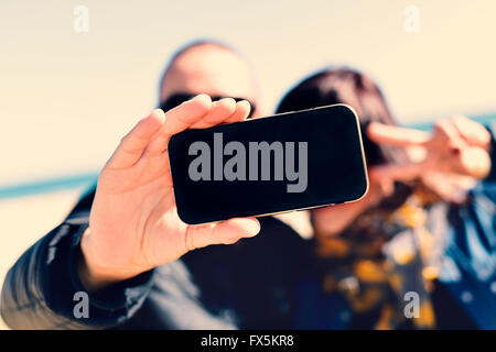 closeup of a young man and a young woman taking a self-portrait with a smartphone while she is doing the victory sign, in front Stock Photo