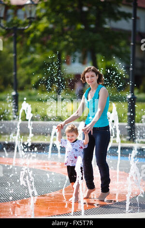 Mother with her son playing in a fountain at summer day Stock Photo