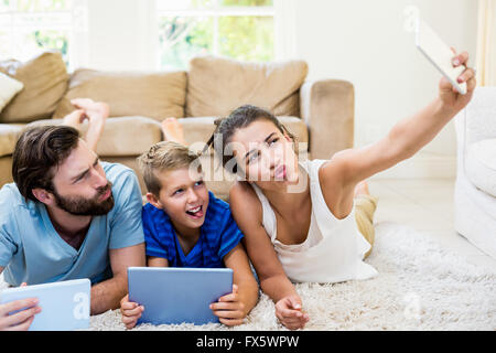 Parents and son lying on rug and taking selfie from phone Stock Photo