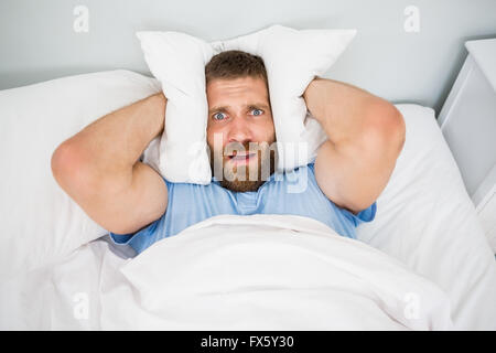 Man covering ears with pillow in bed Stock Photo