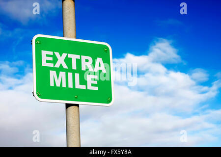 Green extra mile sign against a blue sky Stock Photo