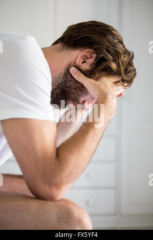 Worried man with hand on forehead sitting on bed Stock Photo