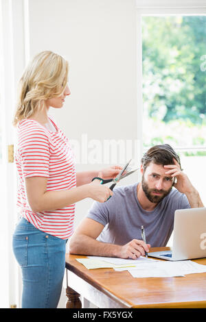 Woman cutting a credit card while tense man with bills sitting at table Stock Photo