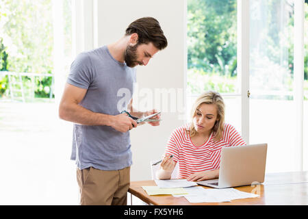 Man cutting a credit card while tense woman with bills sitting at table Stock Photo