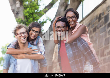 Young men giving piggyback to women Stock Photo