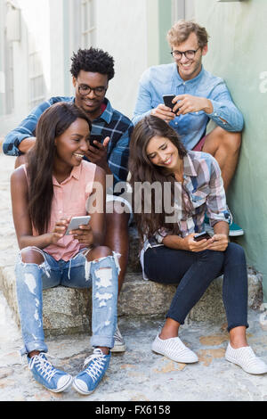 Friends sitting together using mobile phone Stock Photo