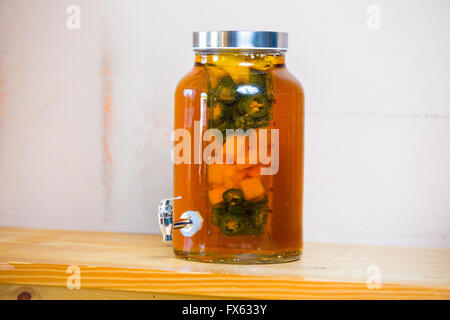 Tequila infused with jalapeno peppers in a tea jar at a restaurant bar. Stock Photo