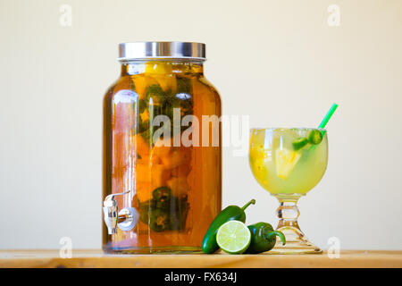 Tequila infused with jalapeno peppers in a tea jar at a restaurant bar. Stock Photo