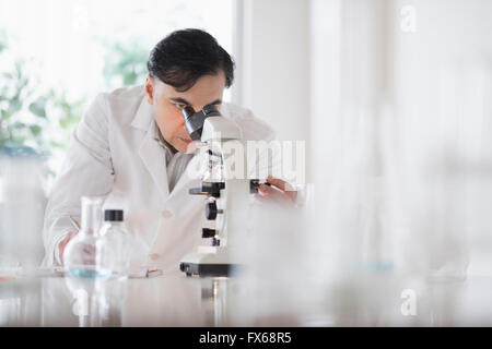 Mixed race scientist using microscope in laboratory Stock Photo