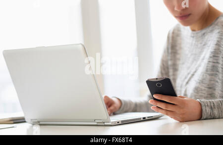Hispanic woman using cell phone and laptop Stock Photo