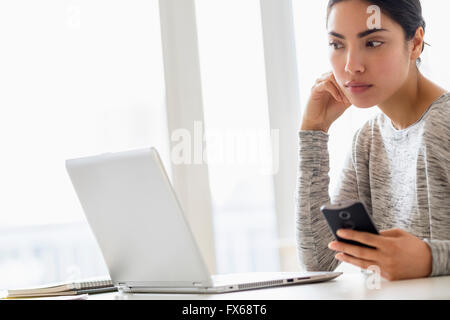 Hispanic woman using cell phone and laptop Stock Photo