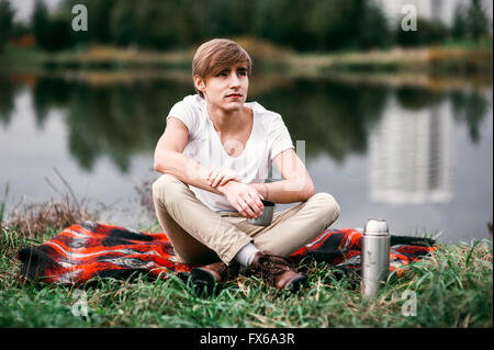 Caucasian man sitting near rural pond Stock Photo