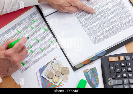 Busy financier cross checking two sales reports with a calculator and some money laying on his desk Stock Photo
