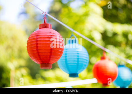 Red and blue paper lanterns hung up high for an outdoor wedding reception. Stock Photo