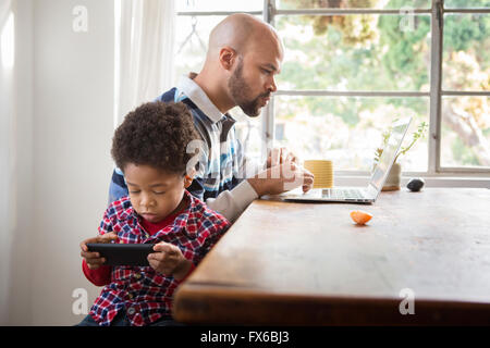 Mixed race father and son using technology at table Stock Photo