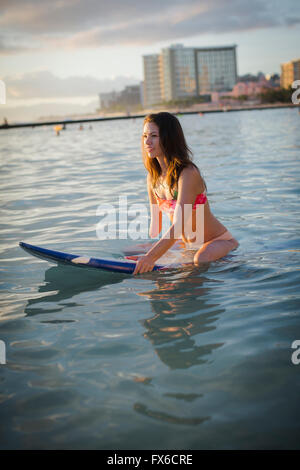 Mixed race amputee sitting on surfboard in ocean Stock Photo