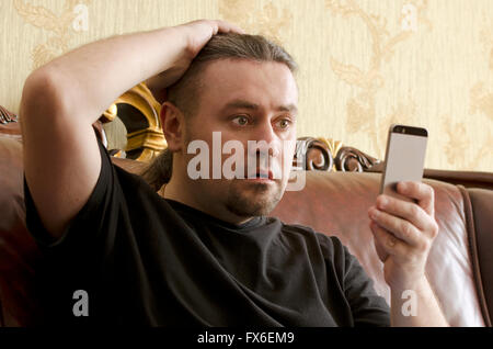 surprised man looking at cell phone while sitting on a sofa Stock Photo
