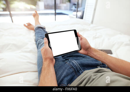 Closeup image of man lying on a bed holding a blank digital tablet. POV shot of man relaxing in bedroom using touch screen compu Stock Photo