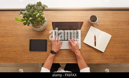 Directly above view of human hands typing on laptop. Laptop, digital tablet, diary, coffee cup and potted plant on work desk. Ma Stock Photo