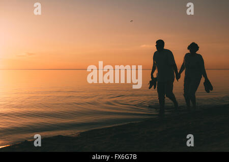 Silhouette of adult couple walks on the seashore against a sunset. Stock Photo