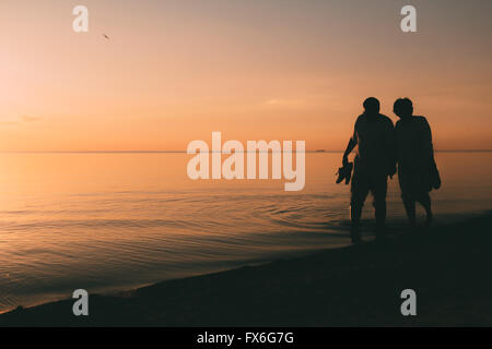 Silhouette of adult couple walks on the seashore against a sunset. Stock Photo