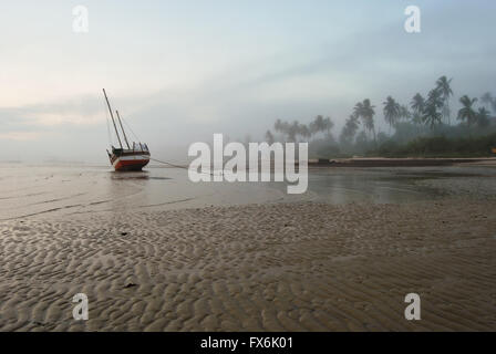 On a beach in Vilankulos, a lone dhow rests in the misty morning calm of low tide just before sunrise brings it to life. Stock Photo