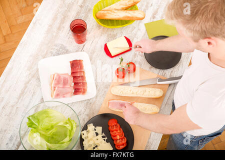 A young man preparing a sandwich in the kitchen. Stock Photo