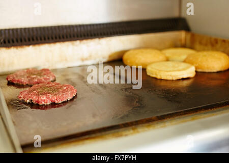 Burger patties frying on a grill with open buns toasting Stock Photo