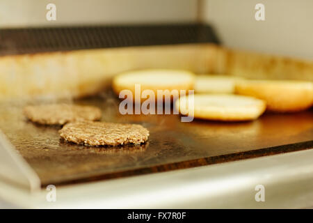 Burger patties being fried alongside open toasted buns Stock Photo