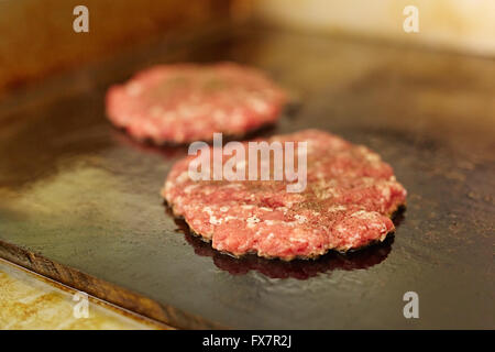 Two fresh burger patties frying on a grill Stock Photo