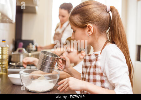 Family cooking background. Mum and children in the kitchen sieving flour Stock Photo