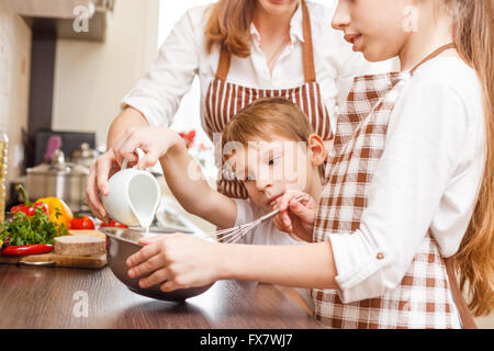 Mother with children cooking scrambled egg or omelette in the kitchen. Family cooking background Stock Photo