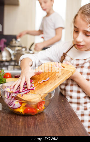 Teenage girl cooking together with her family in the kitchen Caucasian girl putting onion into mixing bowl with salad Family coo Stock Photo