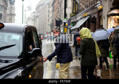 Man & woman about to get into a black taxi in the rain in London Stock Photo