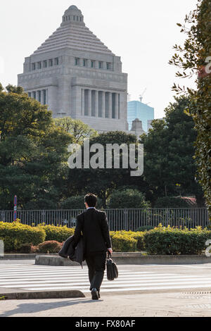 A Japanese office worker or salaryman crosses a road near the Japanese Diet (Parliament) Building, Nagatacho, Tokyo, Japan. Stock Photo