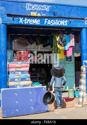 A man wearing a large polythene bowl like a hat in the hot sun outside a fashion shop in Voi Southern Kenya Stock Photo
