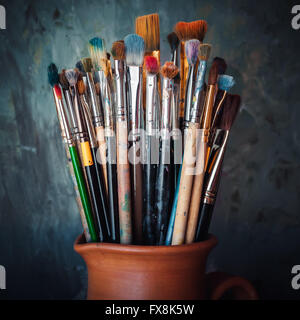 Paintbrushes in a jug from potters clay on dark panting background. Stock Photo