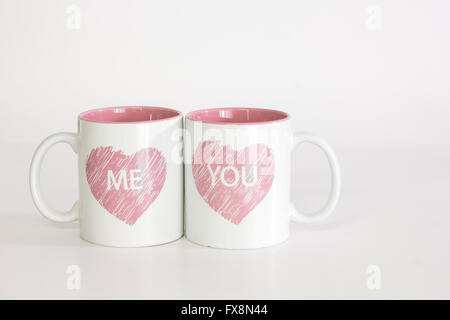Two white coffee mugs with a heart logo pushed close together spelling 'me you'. Isolated against a pure white background Stock Photo