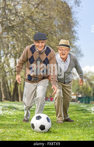 Vertical shot of a joyful senior friends playing football in a park on a sunny spring day Stock Photo