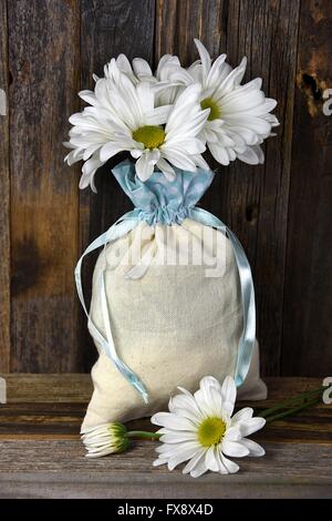 White daisy bouquet in muslin sack with blue satin ribbon on rustic wood. Stock Photo