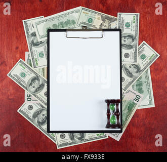 Blank paper sheet in clipboard placed on center of money dollar and wood background, sandglass, business concept and information Stock Photo