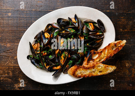 Mussels with parsley and bread toasts on plate on dark wooden background Stock Photo