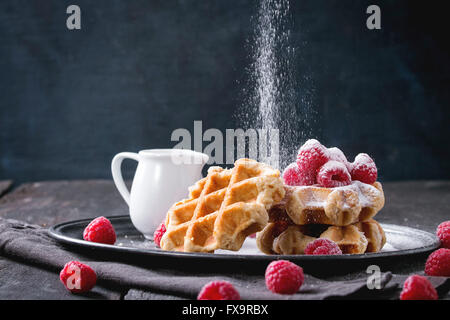 Belgian waffles with raspberries and sieving sugar powder, served with jug of milk on vintage metal tray with textile napkin ove Stock Photo