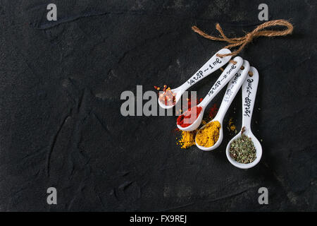 Assortment of ground colorful spices in white different ceramic measuring spoons over black textured background. With copy space Stock Photo