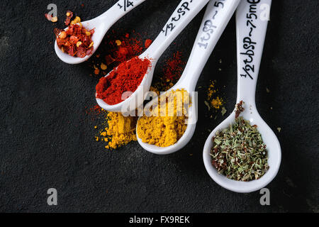 Assortment of ground colorful spices in white different ceramic measuring spoons over black textured background. With copy space Stock Photo