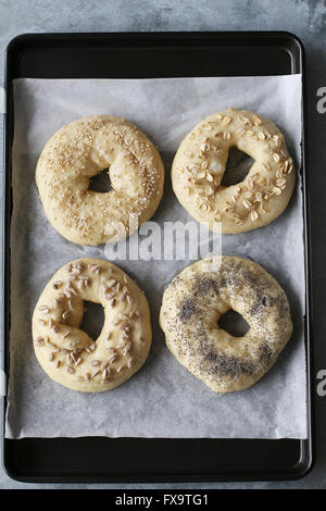 Bagels dough sprinkled with different types of seeds on tray Stock Photo