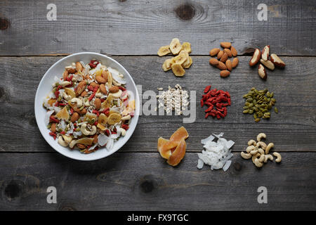 White ceramic bowl full with a healthy trail mix of dried fruits, nuts and seeds. Shot areal view with ingredients seporated and Stock Photo