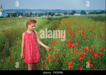 cute girl in red dress walks at poppy field Stock Photo